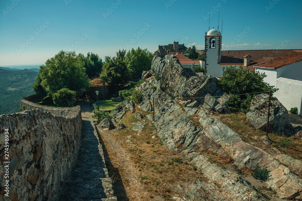 Church steeple and houses with whitewashed wall over rocks in Marvao