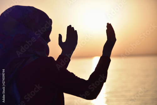 Muslim woman praying in the ship praying at sunset with hands up. A silhouette of islamicwoman  praying at sunset fom the big ship.
