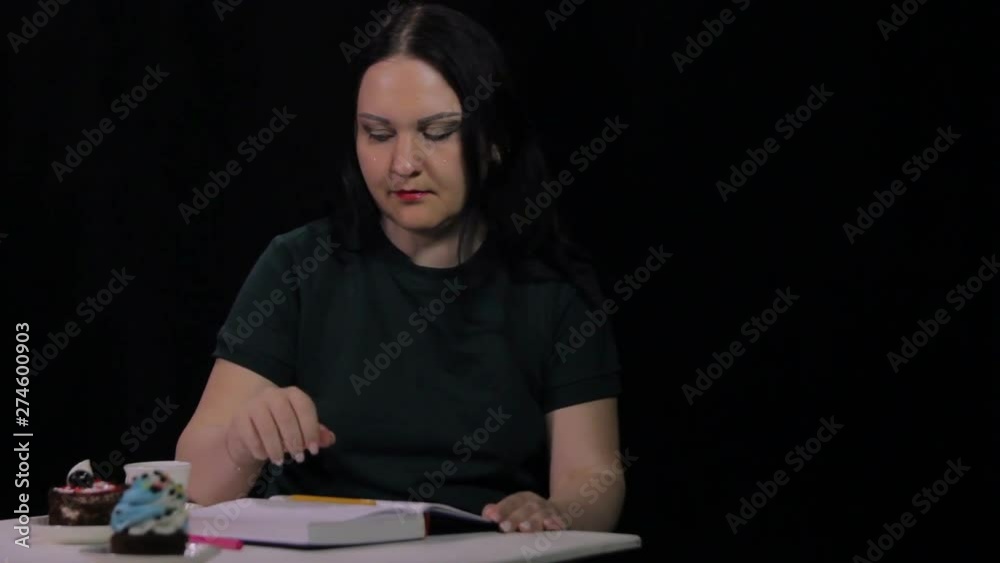 A woman in a cafe drinks coffee from a white cup on a black background and writes in a diary A woman in a cafe drinks coffee from a white cup on a black background and writes in a diary