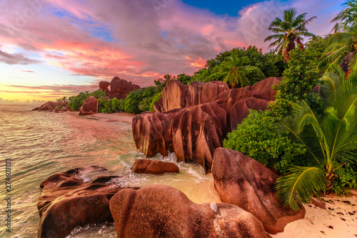 Dramatic colorful sky at twilight at scenic Anse Source d'Argent Beach in Seychelles, La Digue. Aerial view of amazing landscape with huge shaped rock stone of granite and palm trees.