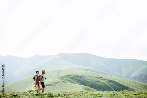 Couple walking with backpacks on the green meadow  traveling in the mountains during the summer time  wide landscape view