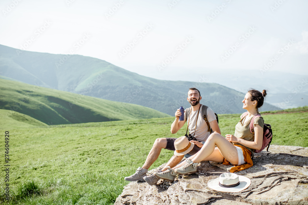 Young couple drinking water while resting on the rock during the travel in the mountains