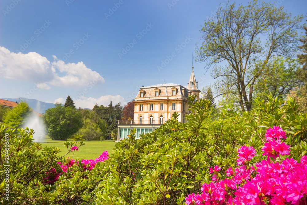 spring landscape with pink flowers and beautiful villa house with fountain in bright day blue sky background.