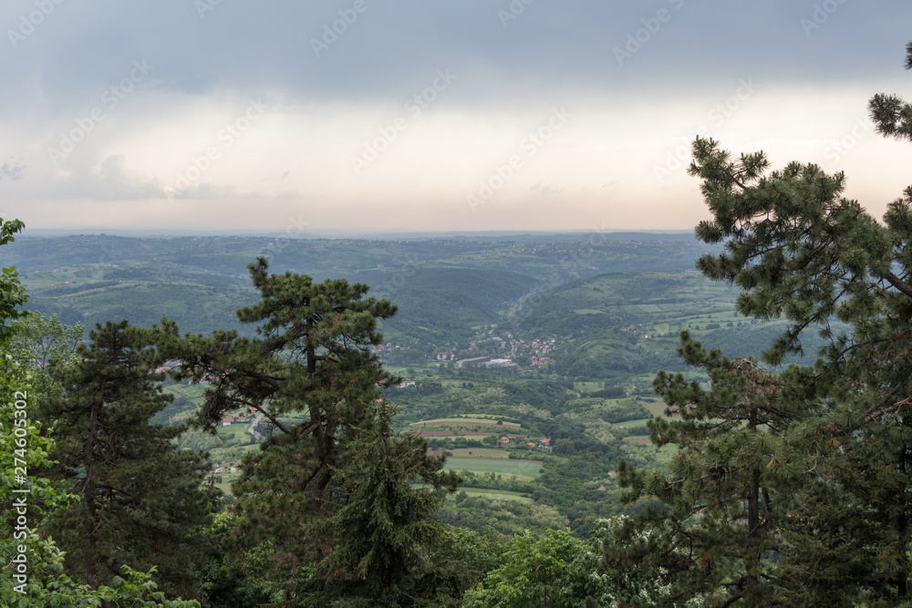 Panorama view over the lush green hills and some villages on the outskirts of Belgrade, Serbia. Moody sky. Nature scenery. Nature background.
