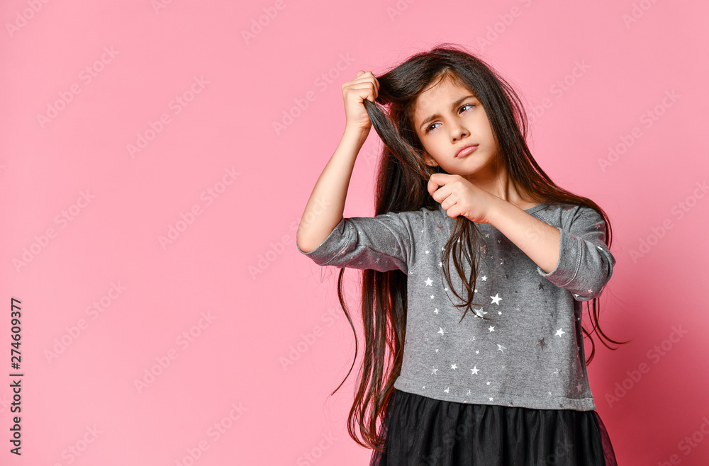 little brunette girl with long hair holds a strand of her hair and looks at it. Hair care and haircut. little brunette girl with long hair holds a strand of her hair and looks at it. Hair care and haircut.