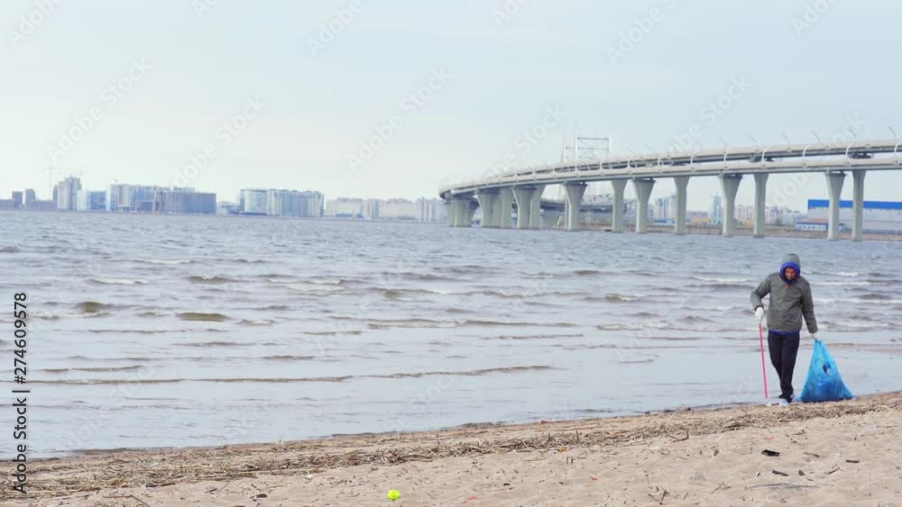 Lockdown side view of two young environmental activists using trash pickers and bags to collect waste on polluted sea beach