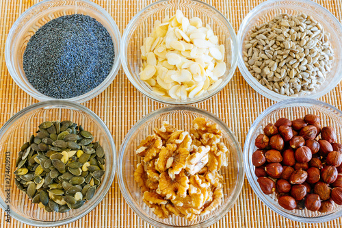 Small glass bowls with poppy seeds, sliced almonds, sunflower seeds, walnuts, hazelnuts, and pumpkin seeds.