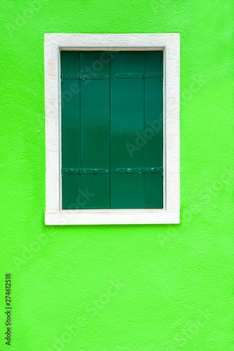 Window with green shutters on the green wall. Colorful architecture in Burano island, Venice, Italy.