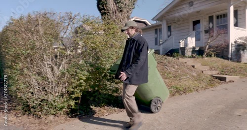 Man walking his trash can down to the end of the curb during the winter