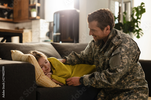 Small girl sleeping carelessly on the sofa while military dad is next to her. © Drazen
