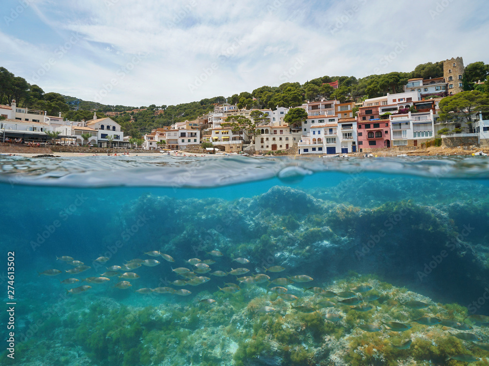Spain village on Mediterranean coast with fish underwater, Sa Tuna cove, Begur, Costa Brava, Catalonia, split view half over and under water