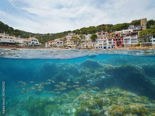 Spain village on Mediterranean coast with fish underwater, Sa Tuna cove, Begur, Costa Brava, Catalonia, split view half over and under water