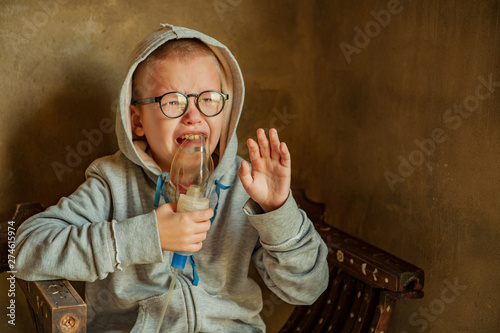 Cute little boy from school for children with poor eyesight holds inhaler in his hands to spray medication. Unhappy chilld cries intensely with tears and snot. Shallow focus photo