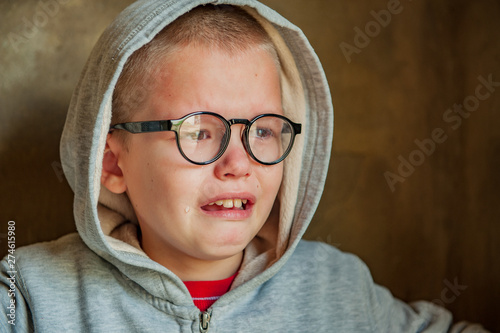 Cute little boy from school for children with poor eyesight holds inhaler in his hands to spray medication. Unhappy chilld cries intensely with tears and snot. Shallow focus photo