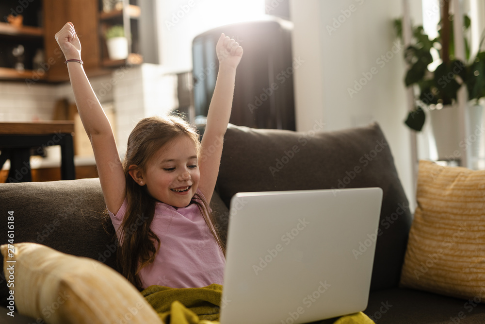 Cheerful small girl celebrating while using laptop at home. Cheerful small girl celebrating while using laptop at home.