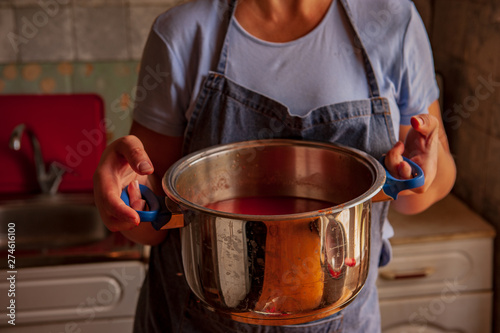 woman cook in an apron prepares tomatoes in a saucepan, rubs through a sieve and prepares tomato juice. Female hands closeup.