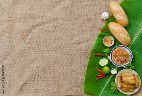 Vietnamese blank food background with Banh Mi, spring roll and shrimp dumpling on a green banana leaf and sedge fabric photo