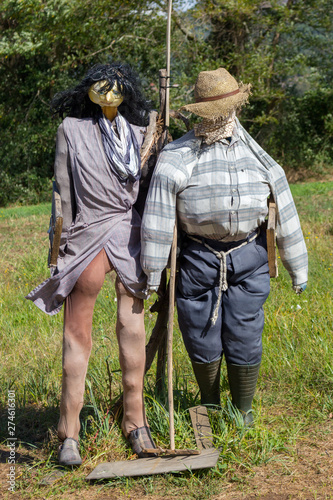 Two funny scarecrows in the field. Pair of scarecrows with hat and stick. Harvest protection and security concept. Rural landscape. Farm guard. Outdoor security dolls in meadow.