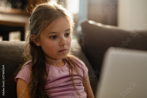 Pensive little girl using laptop while relaxing at home.