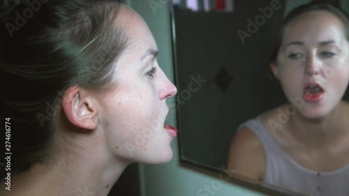 This slow motion video shows a sick and troubled young woman looking into a dirty bathroom mirror and spitting blood.