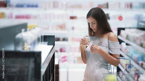Pretty girl chooses perfume in cosmetics shop, sniffs it, slow motion