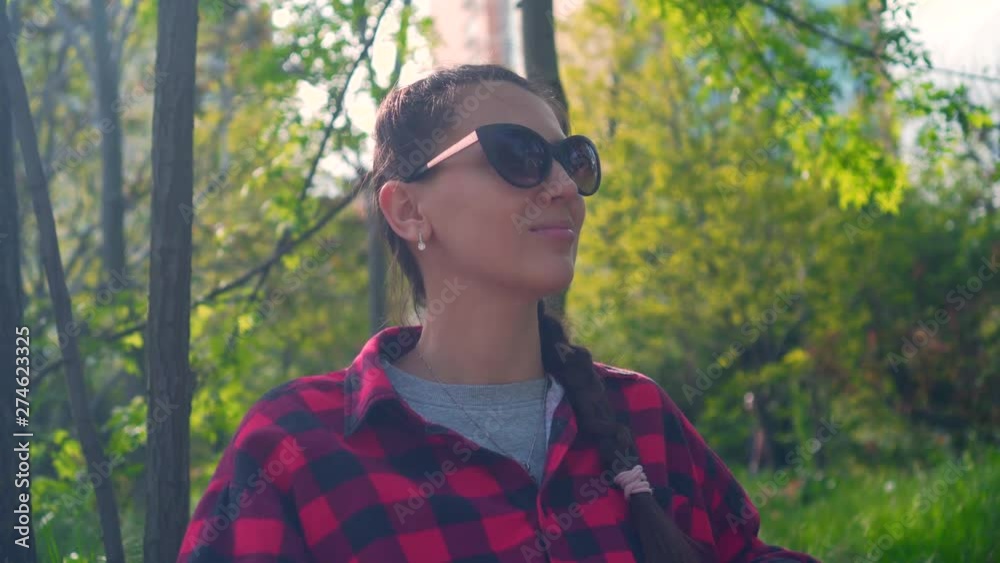 A young and pretty girl is sitting on a bench in a street park. The girl is dressed in a black and red shirt and sunglasses. A young and pretty girl is sitting on a bench in a street park. The girl is dressed in a black and red shirt and sunglasses.