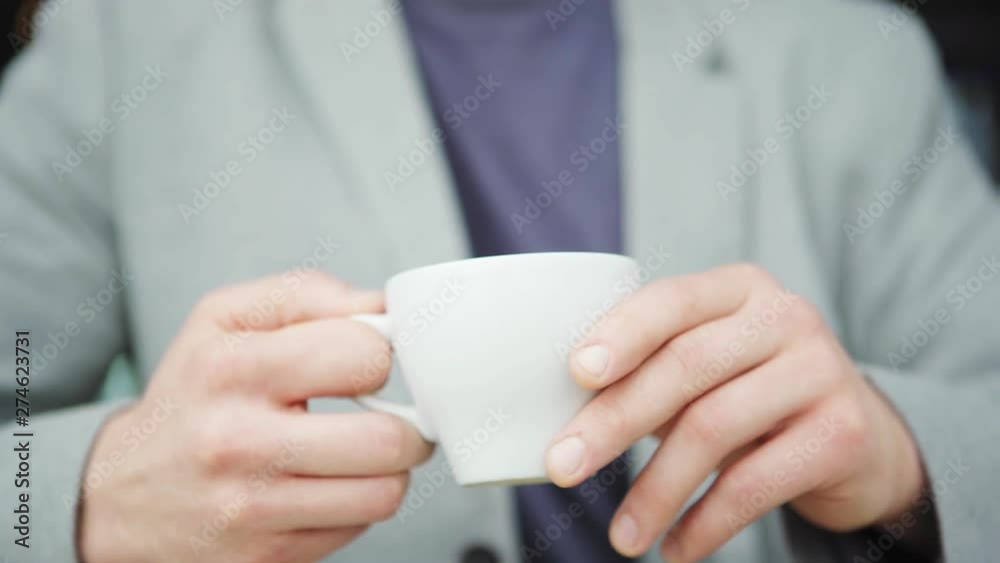 Tracking right closeup of unrecognizable man standing outdoors and holding white coffee cup in his hand