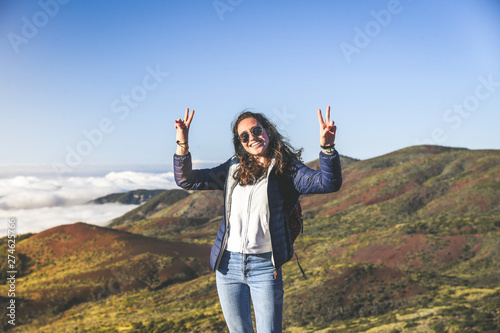 Smiling teenager with raised hands standing on the top of the mountain. Gorgeous view to forest sea and clouds in background. Volcano Teide  Tenerife Spain. Adventure freedom tourism and youth concept