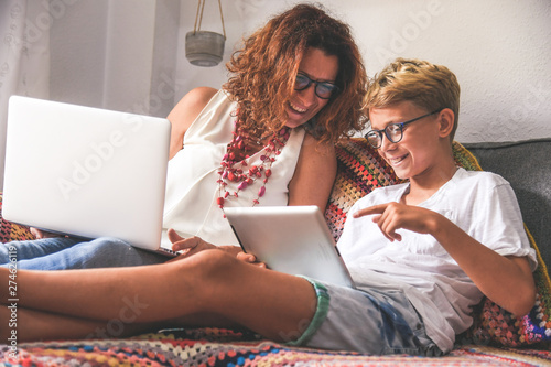 Beautiful teen reading new trend stories online on tablet with mum. Technology addicted young boy watching social video at home with his mother. Child and mommy communicate and plays with tech device.