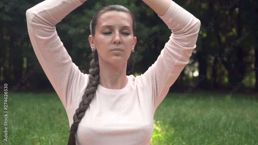A pregnant woman practices yoga in the park while sitting on a rug, sitting in a lotus position, holding her arms above and meditating. Relaxing and being in a light lotus.