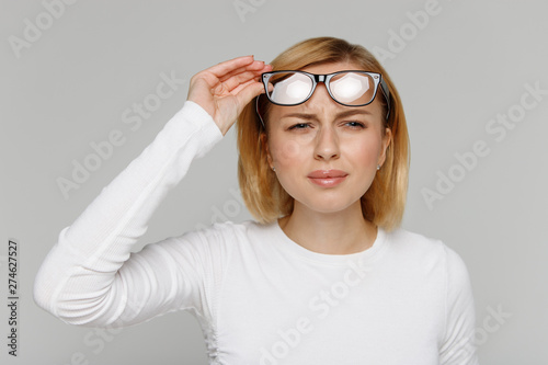 Woman has problems with poor eyesight, squinting while trying to see something, taking off glasses, isolated on grey background. Myopia, hyperopia, vision concept. photo
