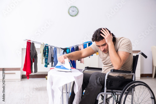 Young man in wheel-chair doing ironing at home 