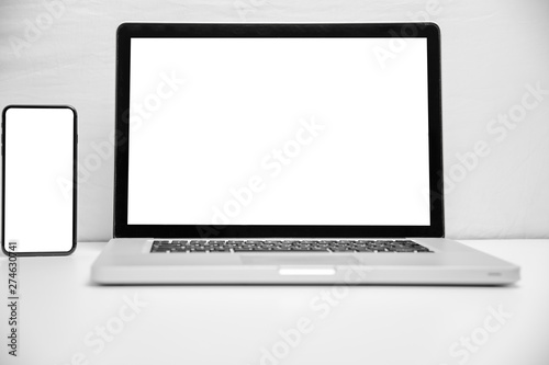 Laptop with blank screen on white table with smartphone with blank screen. Home interior or office background