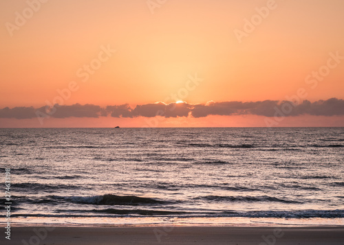 Risen Sun Hidden in Clouds Along the Horizon as Boat Sails Past