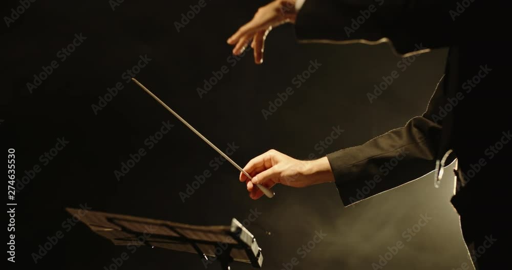 Close up shot of hands of symphony orchesra conductor directing music by waving his baton. Studio shot on black background 4k footage