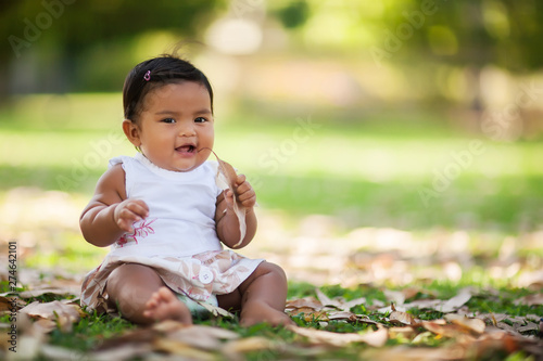 Little baby girl with a smile and grasping a dried leaf and putting it to her mouth for chewing.