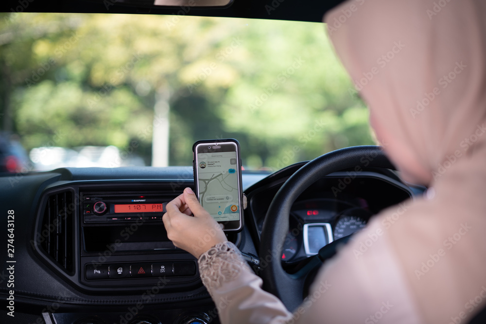A happy young Asian Muslim woman using navigation maps on smartphone to other destination, ride sharing, preparation before driving, female driver transportation concept. A happy young Asian Muslim woman using navigation maps on smartphone to other destination, ride sharing, preparation before driving, female driver transportation concept.