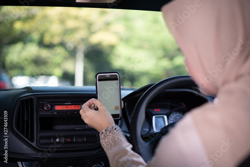 A happy young Asian Muslim woman using navigation maps on smartphone to other destination, ride sharing, preparation before driving, female driver transportation concept.