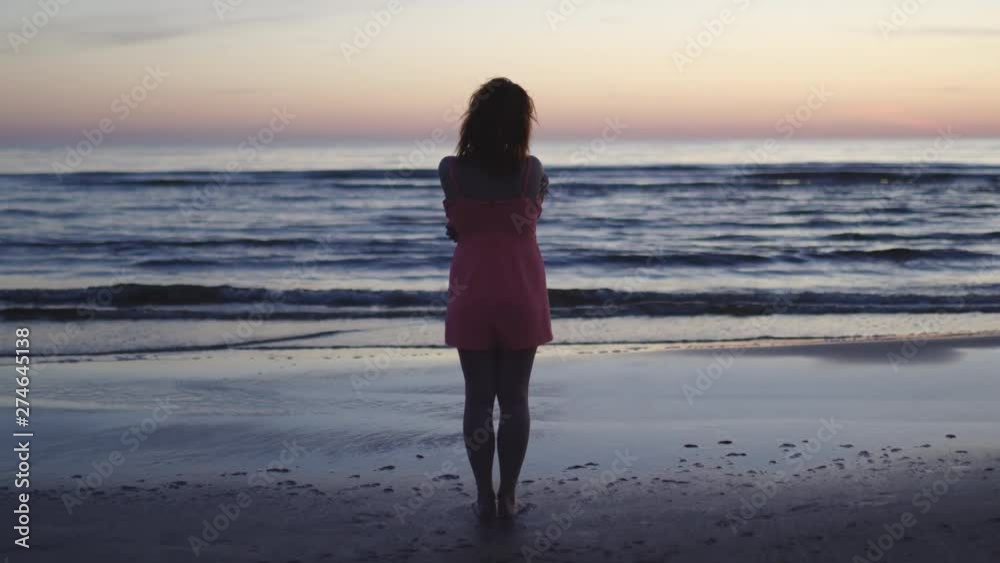 Young woman in bright tender red dress standing on the water enjoying life and nature far away background at the Sunset Young woman in bright tender red dress standing on the water enjoying life and nature far away background at the Sunset