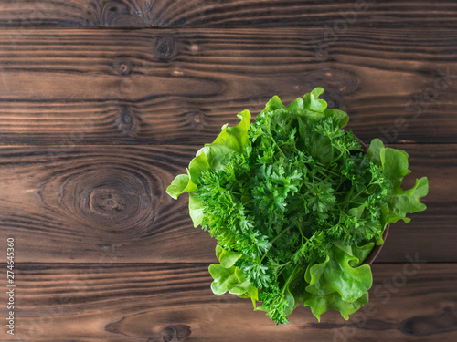 Lettuce and parsley in a bowl on a wooden table with a fork. Flat lay.