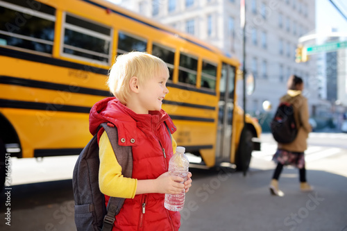 Pupil with schoolbag and bottle of water with yellow school bus on background.