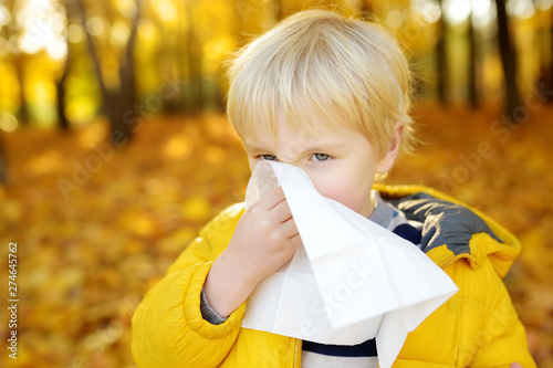 Canvas Print Little boy sneezing and wipes nose with napkin during walking in autumn park
