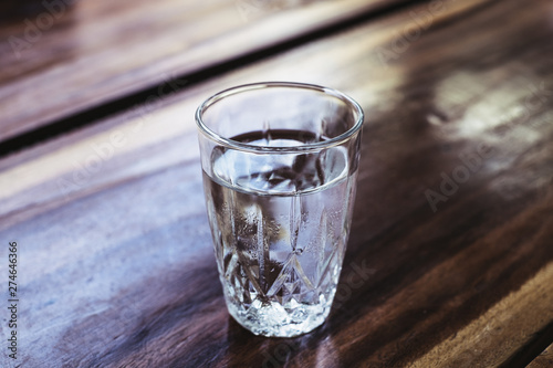 Full clean drinking glass of water on a wooden table. Water is essential to body's cells to function. Selective focus. Copy space. 