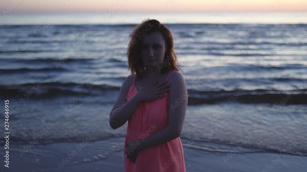 Young woman in bright tender red dress standing on the water enjoying life and nature far away background at the Sunset Young woman in bright tender red dress standing on the water enjoying life and nature far away background at the Sunset
