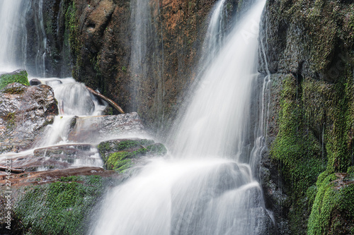 close up details of waterfall stream. rapid flow with long exposure. wet mossy boulders. fallen foliage branches and sticks. refreshing nature background. 