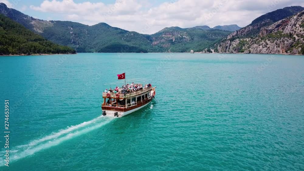 Aerial view: sightseeing boat with tourists sailing on the reservoir Green Canyon Antalya Turkey with clear turquoise water surrounded by mountains and forest.