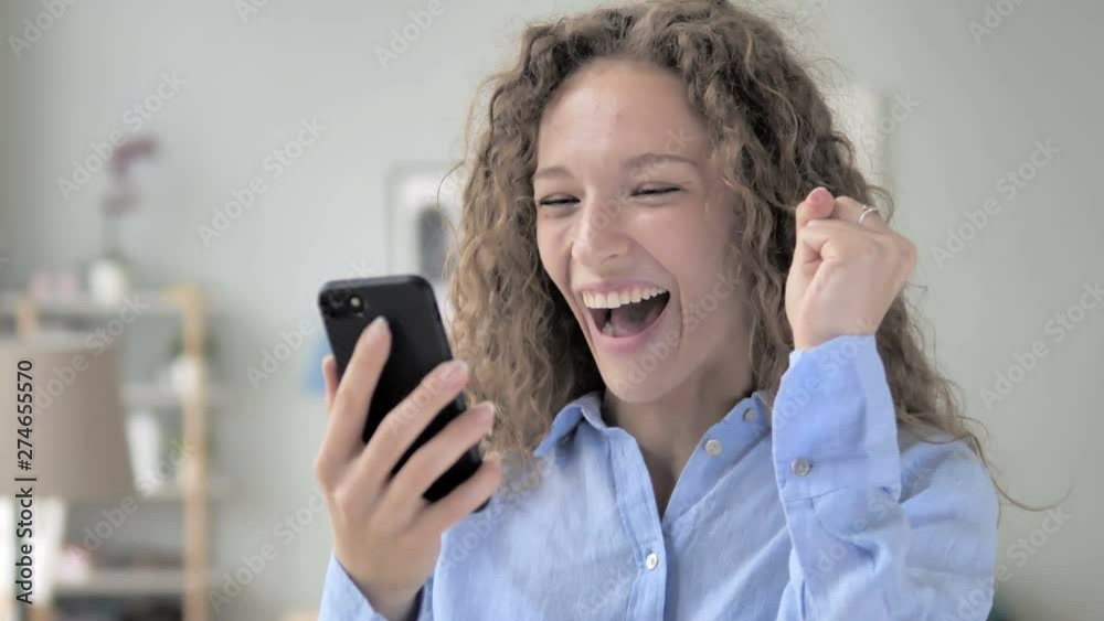 Excited Curly Hair Woman Enjoying Success while Using Smartphone Excited Curly Hair Woman Enjoying Success while Using Smartphone