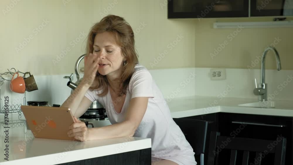 The woman in the kitchen uses the tablet, just woke up. Breakfast. Early morning The woman in the kitchen uses the tablet, just woke up. Breakfast. Early morning