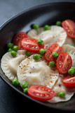 Closeup of ravioli served with cherry tomatoes and green peas, selective focus