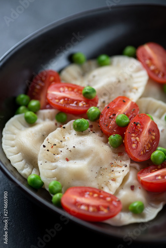 Closeup of ravioli served with cherry tomatoes and green peas, selective focus